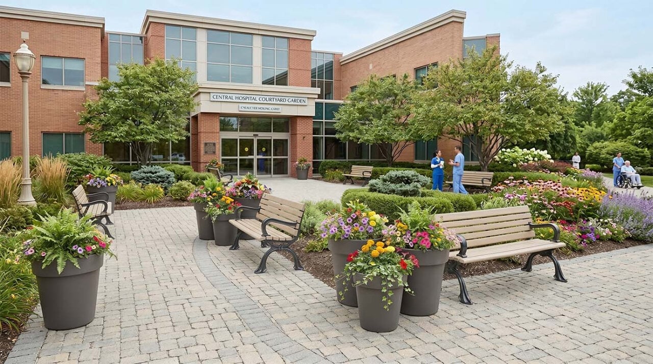 Outdoor hospital courtyard with commercial planters, colourful flowers, and benches creating a welcoming healing garden for patients, visitors, and staff.